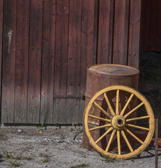 Obraz premium Old yellow tree wheel leaning at a rusty oil barrel, a sunny early summer day in Stockholm