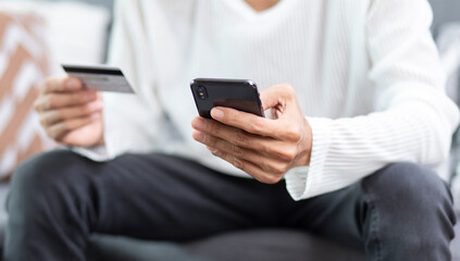 Man using smartphone and holding credit card during sitting at home, online payment application with credit card concept