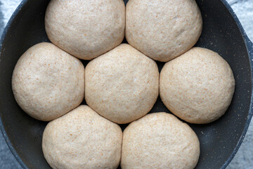 Fototapeta na wymiar Seven raw bread dough rolls in a pan