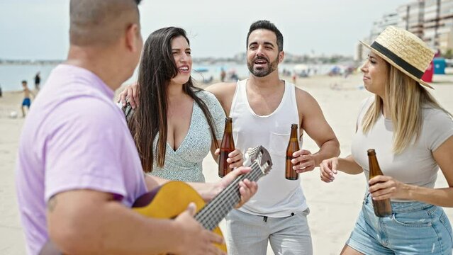 Group of people playing guitar drinking beer dancing at beach