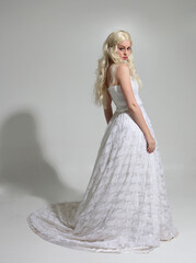 full length portrait of blonde female model wearing long white lace wedding ballgown, walking pose...