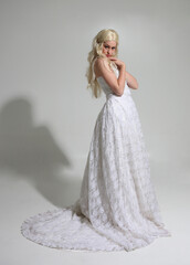 full length portrait of blonde female model wearing long white lace wedding ballgown, walking pose...