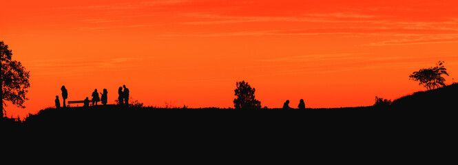 Silhouette of unrecognizable group of people enjoying view and summer sunset on a hill with orange sky in background