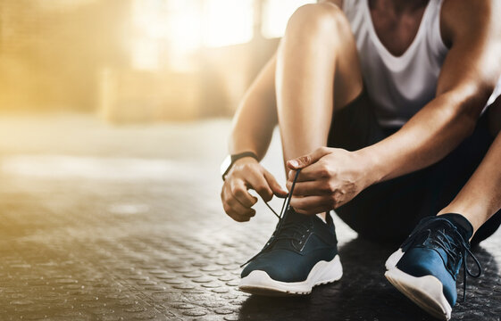 Fitness, gym and man tie shoes before a workout for health, wellness and endurance training. Sports, healthy and closeup of male athlete preparing while tying laces before a exercise in sport center. © Chanel M/peopleimages.com