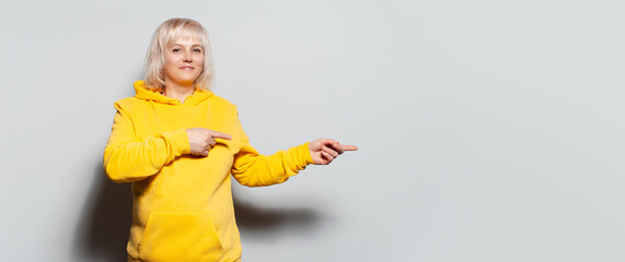 Studio portrait of serious blonde woman in yellow sweater pointing fingers away on copy space of white background. Panoramic banner view.