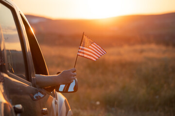 Man in the car holding a waving american USA flag. - obrazy, fototapety, plakaty