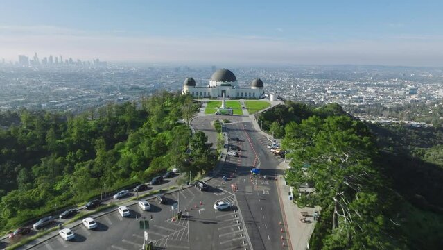 Beautiful aerial shot drone flying above cinematic green lawn of famous landmark Griffith park Observatory Domes building. Sunny summer cityscape on background 4K. Los Angeles California USA Mar 2023