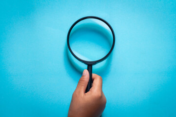 magnifying glass on blue background. hand holding a magnifying glass