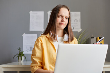 Upset confused woman working on laptop holding phone looking at computer screen having displeased expressing, working on hard freelance project.