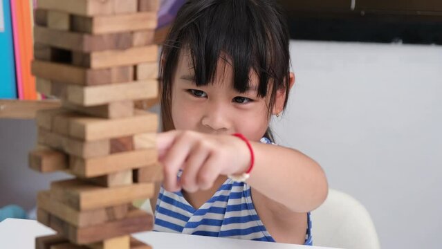 Cute Asian siblings having fun playing Jenga together. Two children playing Jenga board game on table in room at home. Wooden puzzles are games that increase intelligence for children.