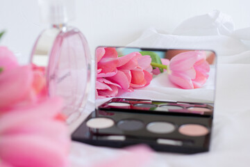 Obraz na płótnie Canvas Pink tulips, eye shadow palette with mirror and perfume bottle on white background, women cosmetics set
