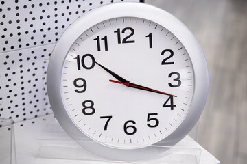 A simple white round wall clock stands and is sold on a shelf in a store.