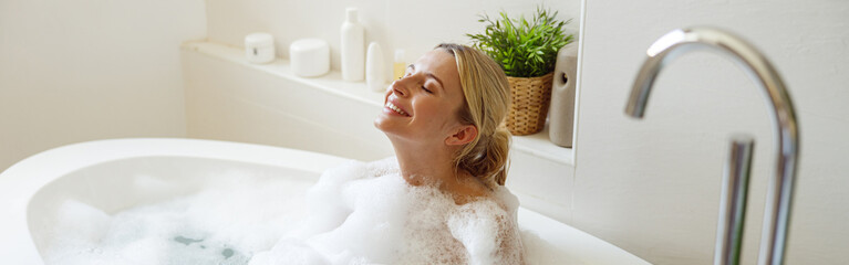 Happy cheerful pretty female enjoying bubbles and hot water in bathtub. Spa and relax day.