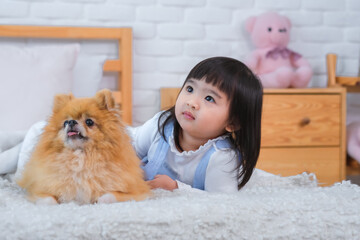 A little girl is sleeping with a dog on the bed in the bedroom while looking away together.