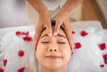 Obraz na płótnie Canvas Beautiful asian woman closed her eyes and smile on her face as the professional masseuse worked on her forehead surrounded by the sweet fragrance of roses in the tranquil spa room.