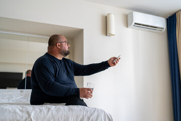 Frustrated overweight man suffering from heat hold glass of water includes conditioning at home....