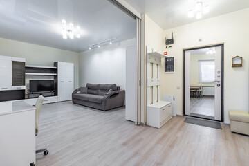 The interior of the kitchen and living room in light white colors with a table, chairs and a TV in a large free space.
