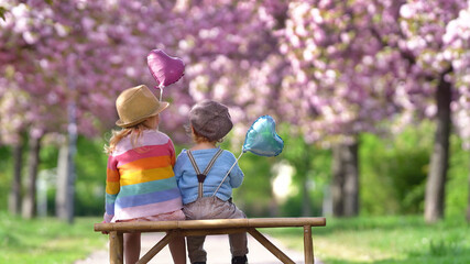 zwei kleine Kinder sitzen unter blühenden Kirschbäumen