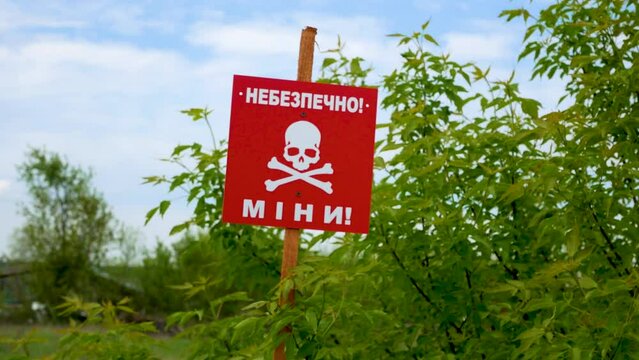 A red skull plaque near a field road that reads Caution, mines. Mine hazard warning. War 2022-2023. Territories mined after hostilities. The concept of humanitarian demining