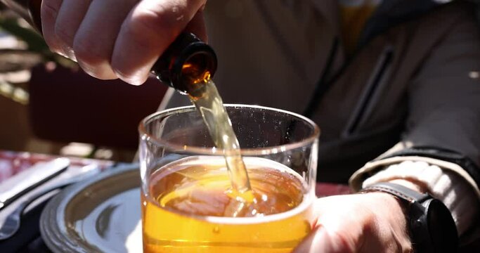 Male hands pour draft beer from bottle into glass. Fresh light foamy beer with gas bubbles