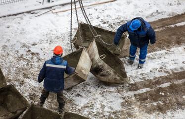 Workers unload containers from concrete from a crane at a construction site