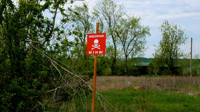 A red sign with the inscription Danger, mines warns of danger in the field near the road in the de-occupied territories. Russian-Ukrainian War 2022-2023