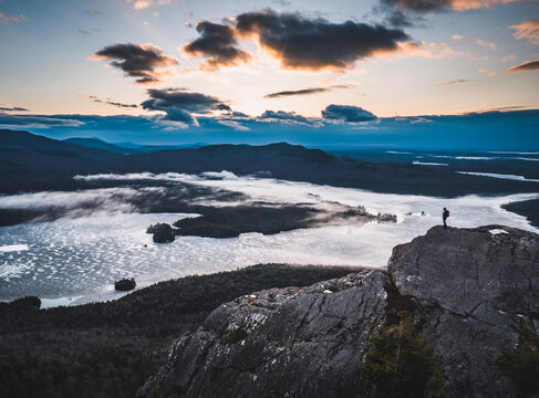 lone hiker stands on rocky summit with lakes and mountains, sunrise