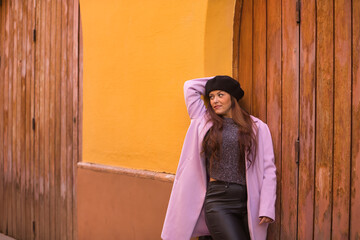 Fototapeta premium Young woman, beautiful, straight brown hair, sweater, coat and black beret, leaning on a wooden door, happy and carefree. Concept beauty, fashion, autumn, winter, cold.