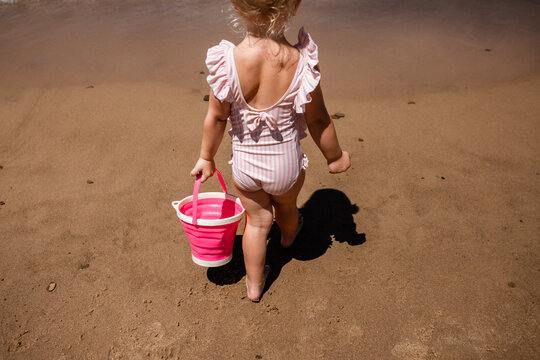 Child on sandy beach walking away with pink bucket on summer vac