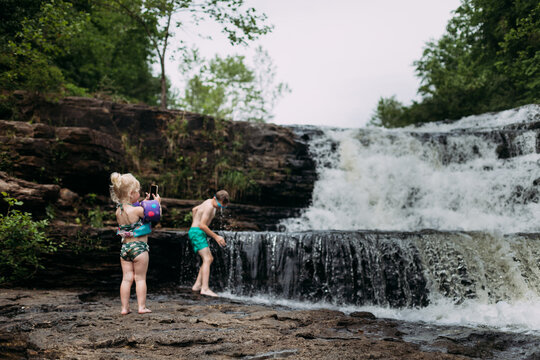 Child taking photos of brother playing in waterfall
