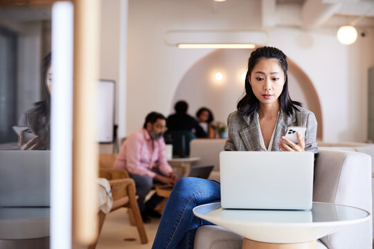 Businesswoman holding smart phone using laptop on table