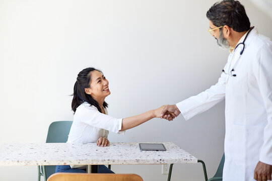 Mature male doctor doing handshake with female patient in clinic