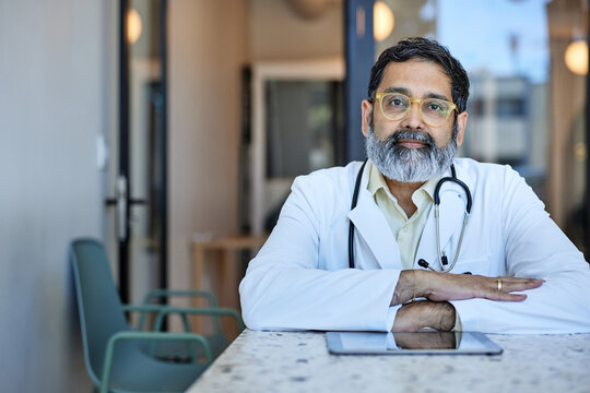 Portrait of male doctor wearing eyeglasses sitting at desk in clinic