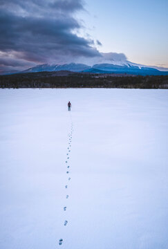 Lone man on lake ice with footsteps and mountain