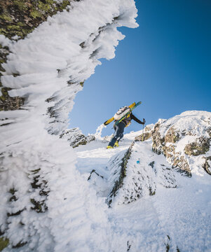 Hiker with skis climbs through snowy ice and rocks on Katahdin, Maine