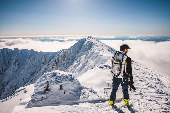 man with backpack stands on snowy summit of Katahdin, Maine in winter