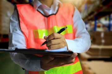 A factory auditor is writing notes on the clipboard during a walk through the warehouse.