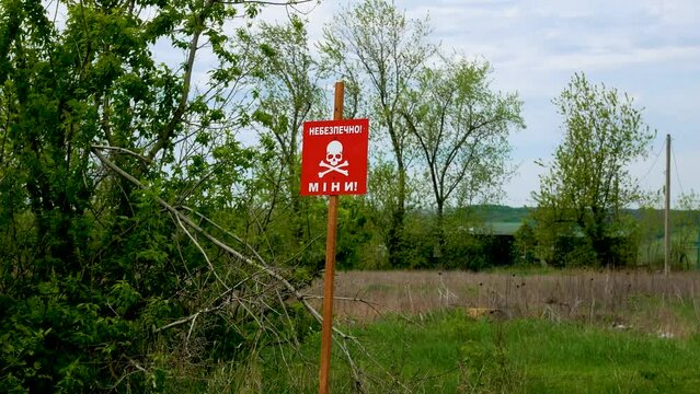 A red sign with the inscription Danger, mines warns of danger in the field near the road in the de-occupied territories. Russian-Ukrainian War 2022-2023