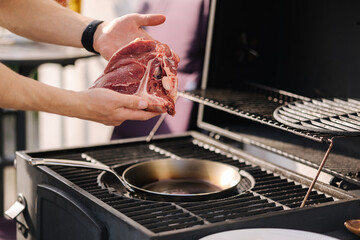 Human hand hold T-bone Steak in front of grill. BBQ concept. Close-up