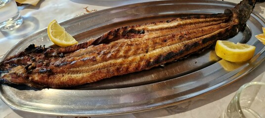 Grilled eel on silver platter on dinner table, served with fresh lemon - water glasses on either side