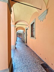 Portico in bright yellow or orange (light) colors in Bologna, Italy, with marble floor and arched stone walls - metal bars in front of window for safety