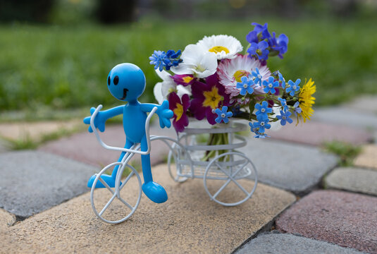 white souvenir bicycle with a bouquet of flowers in a basket and a miniature toy happy man. Birthday card, mother's day with love. atmosphere of love, positivity and joy. Flower delivery