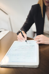 Vertical close-up of a psychologist signing a document on a digital tablet in her office.