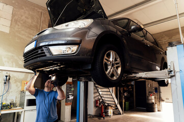 Professional auto mechanic working under a raised car in a car service. specialist examines the car. machine maintenance