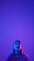 Color light portrait. Amazed girl. Neon surprised woman looking up with interest at advertisement area isolated on blue pink empty space background.