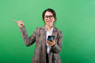 Photo of smiling Asian businesswoman using mobile phone with hands pointing on empty space or copy space for product isolated on isolated green background