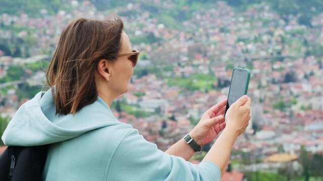 Female tourist taking a picture of cityscape using smartphone. Woman with backpack takes a photo with her cellphone of the blurry aerial view of an old european city.