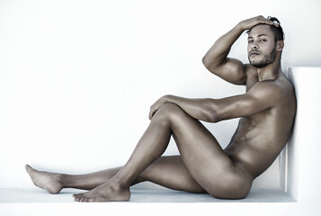 Portrait, nude and a sexy man sitting on the floor of a studio against a white background for...