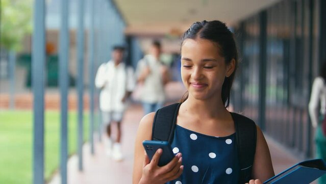 Female high school student walking outside classrooms checking social media or internet on mobile phone - shot in slow motion