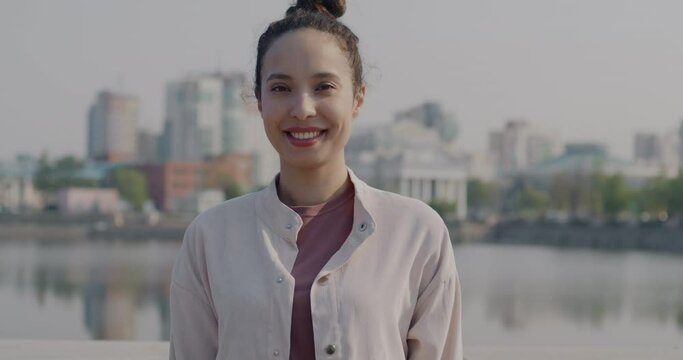 Slow motion portrait of gorgeous biracial woman standing outdoors in rive embankment smiling looking at camera. People and positive emotion concept.